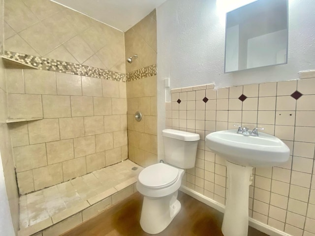 bathroom with a tile shower, hardwood / wood-style floors, tile walls, and toilet