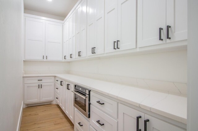 kitchen featuring white cabinets, light stone countertops, oven, and light hardwood / wood-style floors