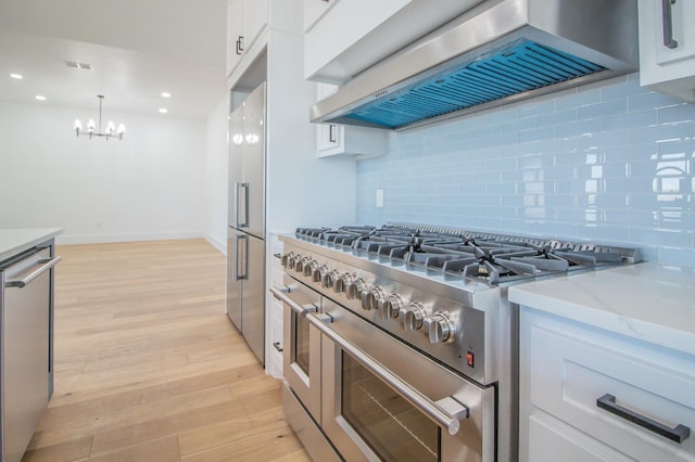 kitchen featuring extractor fan, light stone counters, hanging light fixtures, high quality appliances, and white cabinets