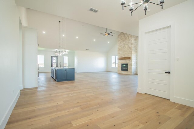 unfurnished living room with sink, high vaulted ceiling, a fireplace, light hardwood / wood-style floors, and ceiling fan with notable chandelier