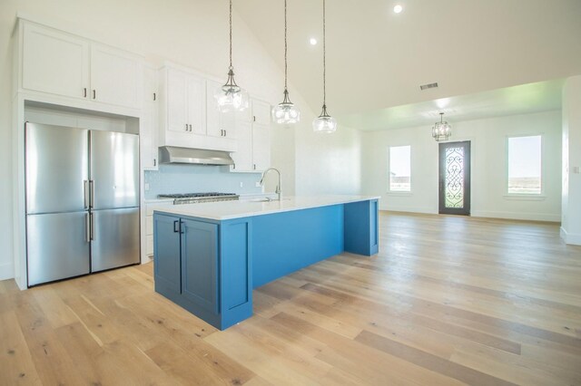 kitchen with stainless steel refrigerator, pendant lighting, an island with sink, and white cabinets