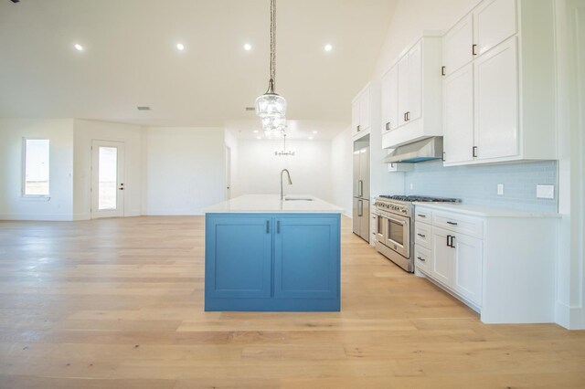 kitchen featuring tasteful backsplash, an island with sink, white cabinets, decorative light fixtures, and range with two ovens