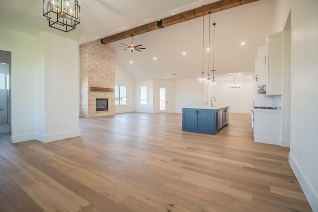 unfurnished living room featuring light hardwood / wood-style flooring, sink, beam ceiling, and a stone fireplace