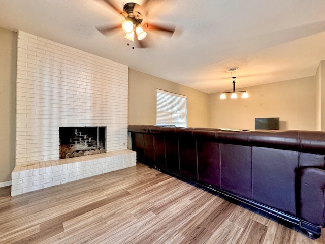 unfurnished living room featuring ceiling fan, light hardwood / wood-style floors, a brick fireplace, and a textured ceiling