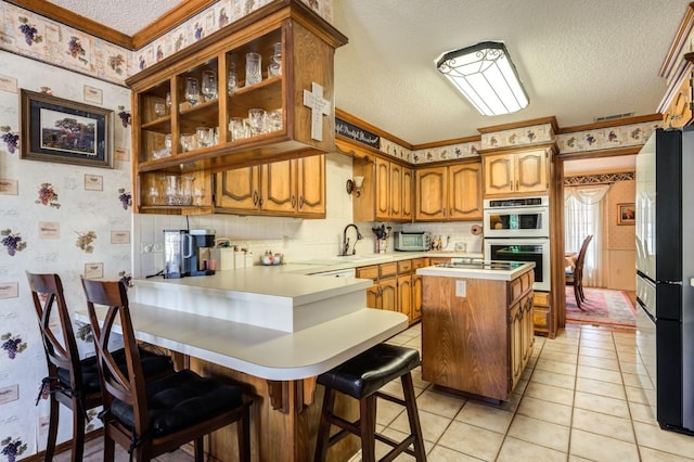 kitchen with a kitchen island, a breakfast bar area, fridge, kitchen peninsula, and stainless steel double oven