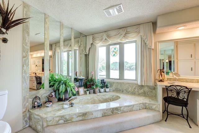 bathroom with a washtub, toilet, a textured ceiling, and a wealth of natural light