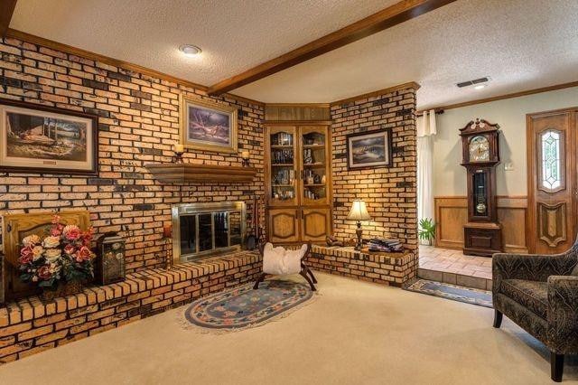 carpeted living room with a brick fireplace, beamed ceiling, ornamental molding, and a textured ceiling