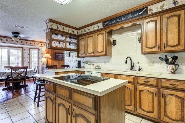 kitchen with black electric cooktop, kitchen peninsula, a textured ceiling, and a kitchen island