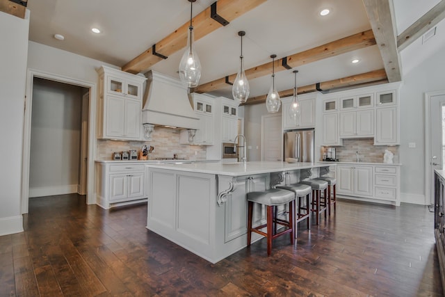 kitchen featuring custom range hood, an island with sink, stainless steel refrigerator, and white cabinets