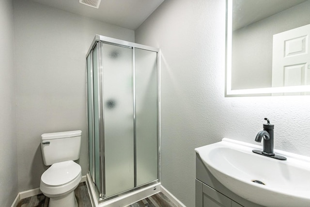 bathroom featuring hardwood / wood-style flooring, vanity, a shower with door, and toilet