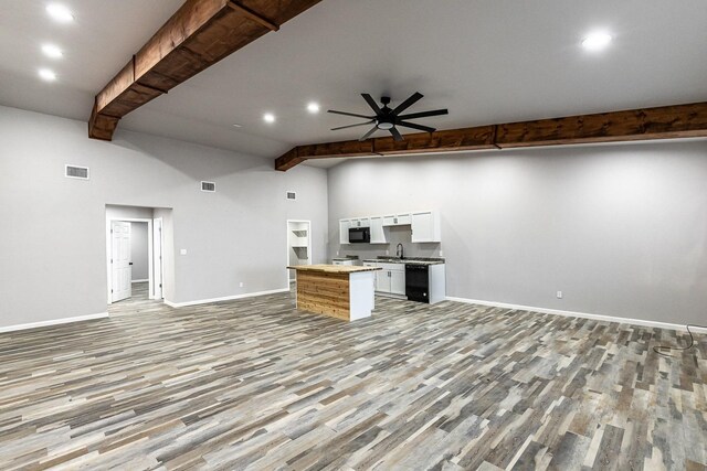 unfurnished living room featuring a towering ceiling, beamed ceiling, sink, ceiling fan, and light hardwood / wood-style floors