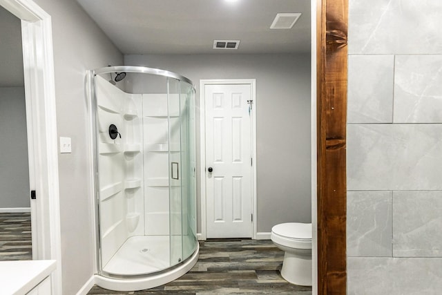 bathroom featuring hardwood / wood-style flooring, a shower with shower door, and toilet