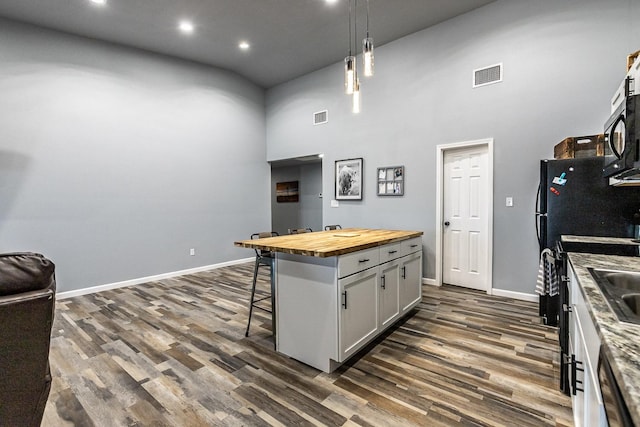 kitchen featuring butcher block counters, a kitchen breakfast bar, hanging light fixtures, a high ceiling, and a center island