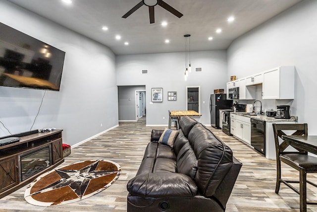 living room featuring ceiling fan, a towering ceiling, sink, and light hardwood / wood-style floors