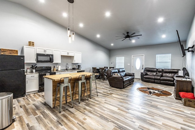 kitchen featuring wood counters, white cabinets, a kitchen breakfast bar, hanging light fixtures, and black appliances