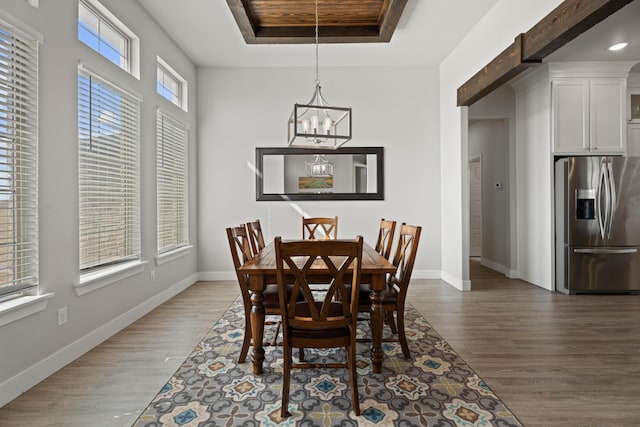 dining space featuring baseboards, a raised ceiling, an inviting chandelier, and wood finished floors