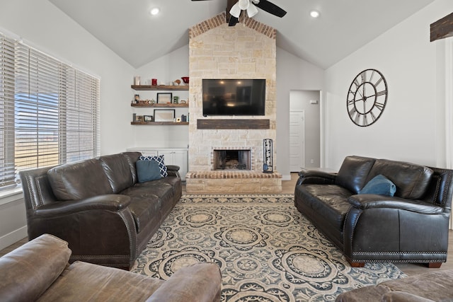 living area with ceiling fan, high vaulted ceiling, a stone fireplace, and baseboards