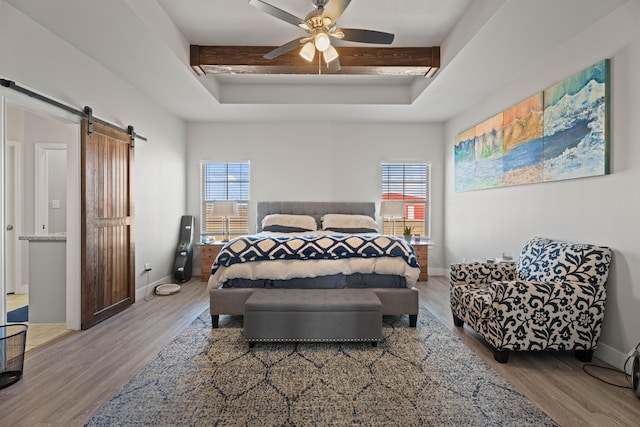 bedroom with a ceiling fan, wood finished floors, a barn door, and a tray ceiling