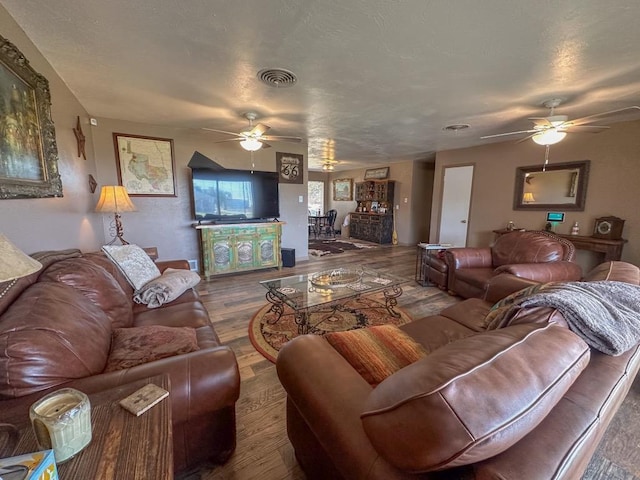 living room with a ceiling fan, visible vents, a textured ceiling, and wood finished floors