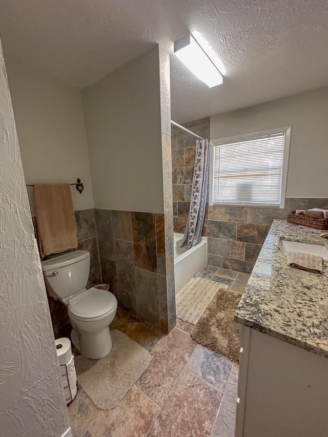 bathroom with a textured ceiling, toilet, tile walls, stone tile flooring, and shower / bathtub combination with curtain