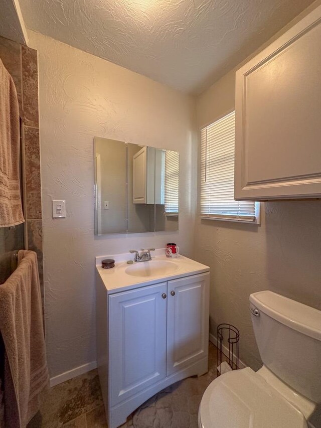 bathroom with toilet, a textured wall, a textured ceiling, and vanity