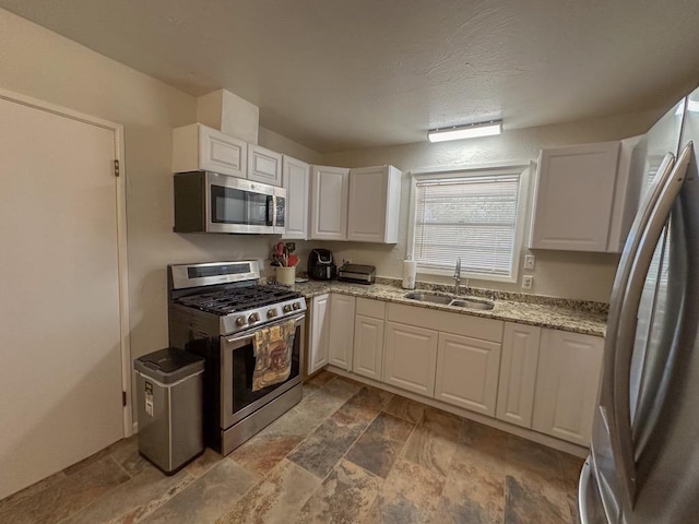 kitchen featuring light stone counters, stainless steel appliances, a sink, white cabinetry, and stone finish flooring