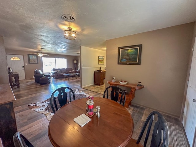 dining space featuring visible vents, a ceiling fan, a textured ceiling, wood finished floors, and baseboards