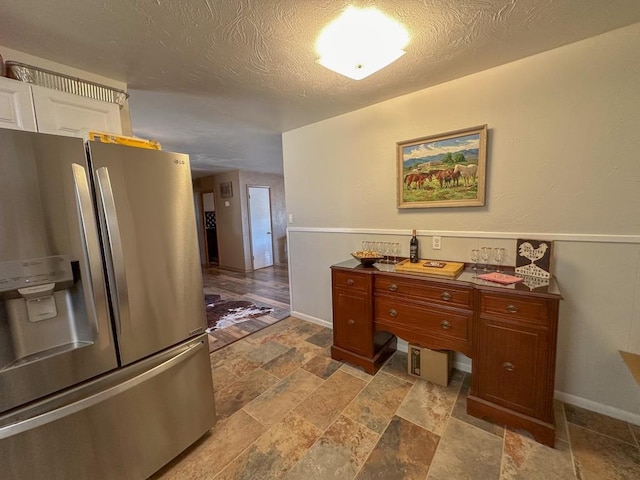 interior space with a textured ceiling, stone finish flooring, stainless steel refrigerator with ice dispenser, and dark countertops