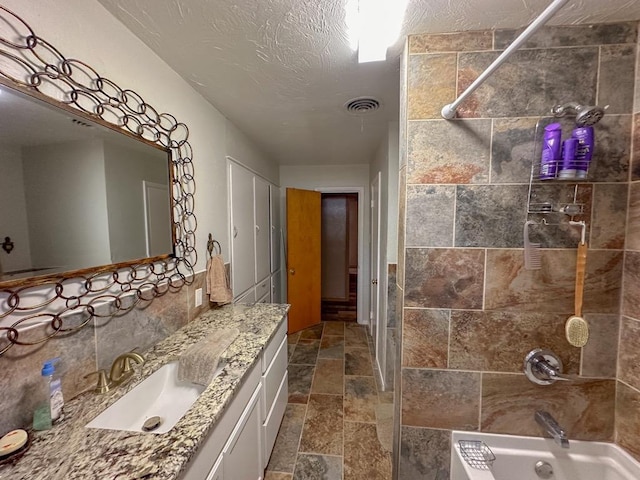 full bath with stone tile floors, visible vents, washtub / shower combination, a textured ceiling, and vanity