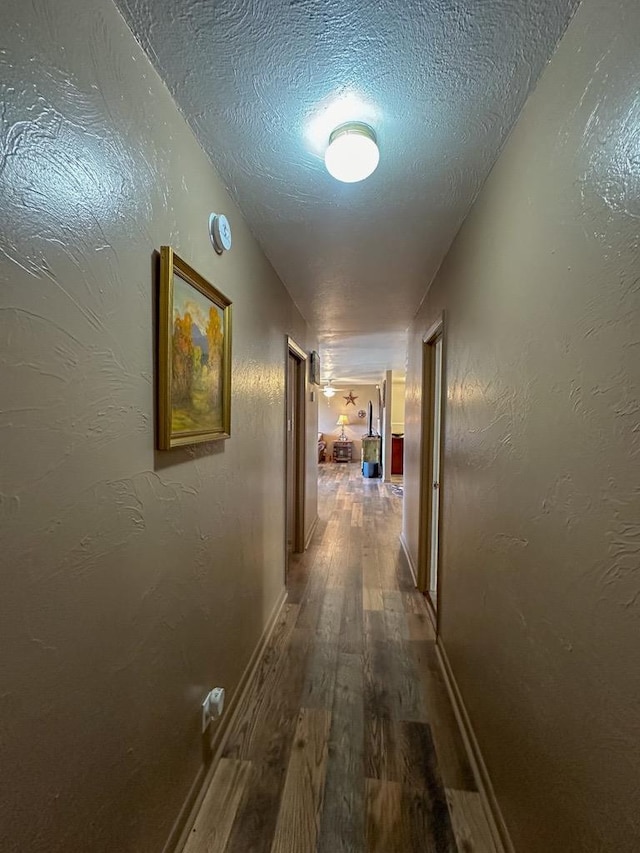 hallway featuring a textured ceiling, a textured wall, wood finished floors, and baseboards