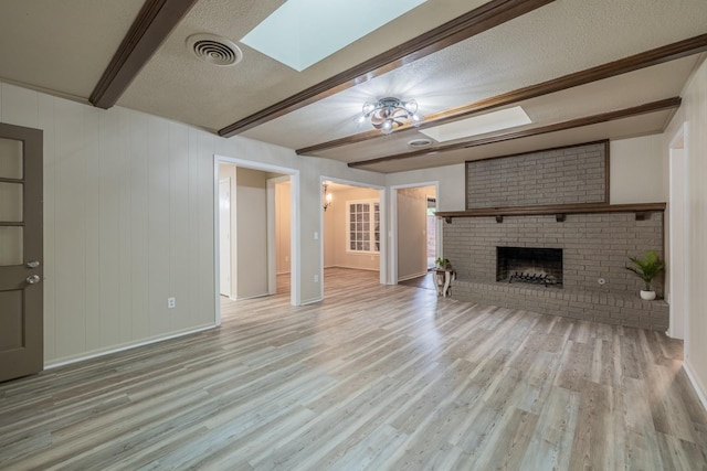 unfurnished living room featuring a skylight, a brick fireplace, a textured ceiling, beamed ceiling, and light hardwood / wood-style floors