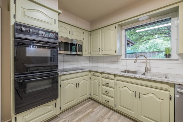 kitchen featuring sink, light hardwood / wood-style floors, cream cabinets, decorative backsplash, and black appliances