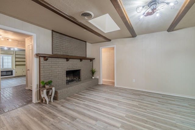 unfurnished living room with a skylight, a brick fireplace, light hardwood / wood-style flooring, an AC wall unit, and beamed ceiling