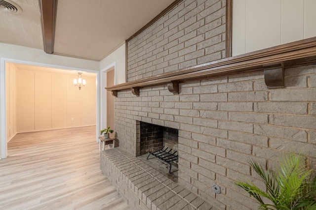 living room with beam ceiling, a chandelier, light hardwood / wood-style flooring, a textured ceiling, and a fireplace