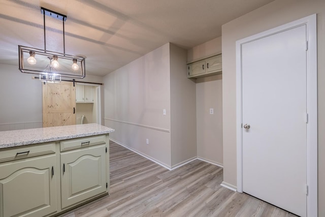 kitchen with hanging light fixtures, light stone countertops, a barn door, and light wood-type flooring