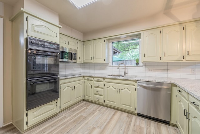 kitchen with sink, light stone counters, black appliances, decorative backsplash, and light wood-type flooring