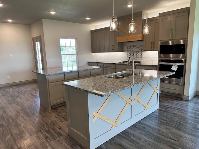 kitchen with sink, dark stone countertops, tasteful backsplash, a center island with sink, and decorative light fixtures