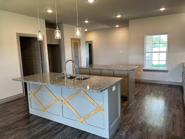 kitchen with pendant lighting, sink, light stone counters, a center island with sink, and dark hardwood / wood-style flooring