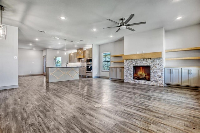 unfurnished living room featuring a stone fireplace, dark hardwood / wood-style floors, sink, and ceiling fan