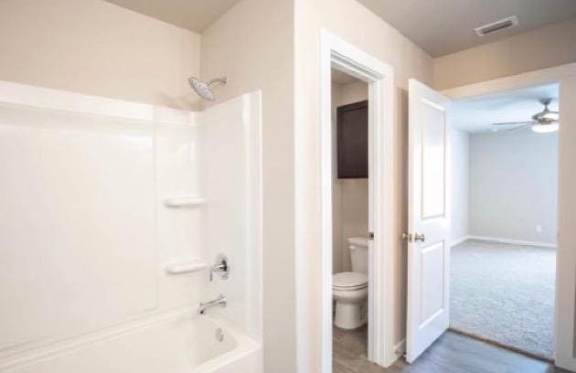 bathroom with bathtub / shower combination, ceiling fan, and toilet