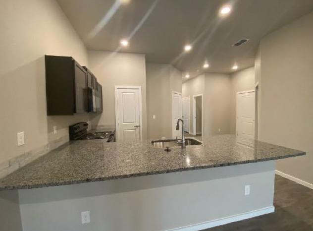 kitchen with range, kitchen peninsula, sink, and dark stone countertops