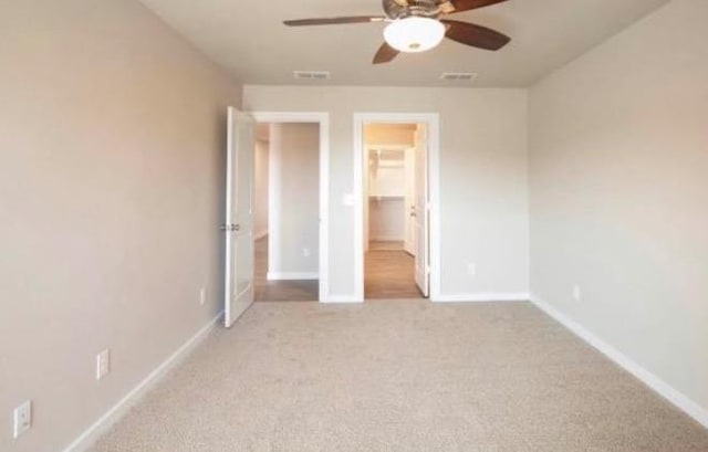 unfurnished bedroom with a spacious closet, light colored carpet, a closet, and ceiling fan