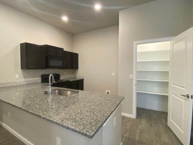 kitchen with light stone countertops, sink, dark wood-type flooring, and kitchen peninsula