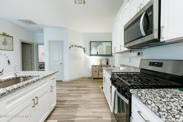 7415 8th St, Lubbock, TX 79416 - kitchen featuring stainless steel appliances, light wood-type flooring, a sink, white cabinets, and light stone countertops