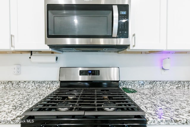 7415 8th St, Lubbock, TX 79416 - kitchen view of gas range oven, stainless steel microwave, white cabinetry, and light stone counters