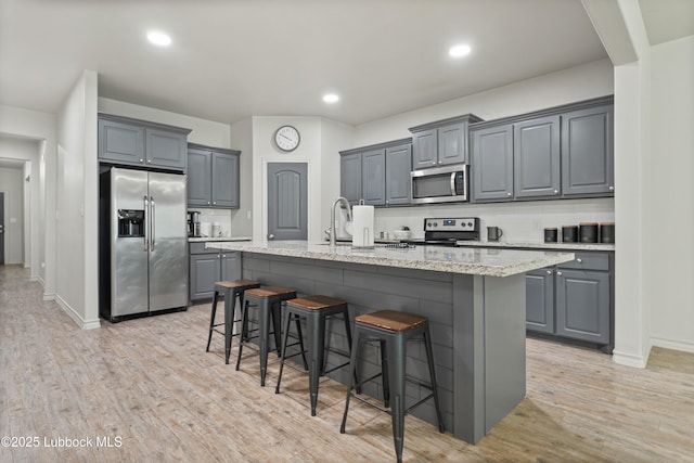 5303 Lehigh St, Lubbock, TX 79416 - kitchen with stainless steel appliances, gray cabinetry, a breakfast bar area, a kitchen island with sink, and light wood-style floors