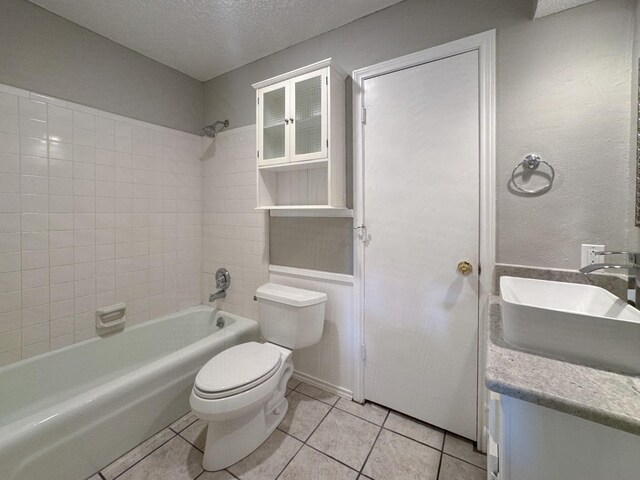 full bathroom with sink, tile patterned flooring, tiled shower / bath combo, toilet, and a textured ceiling