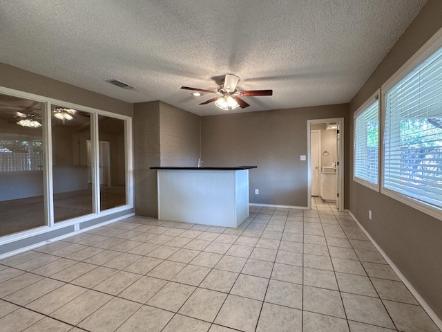 tiled empty room featuring a textured ceiling, ceiling fan, and bar area