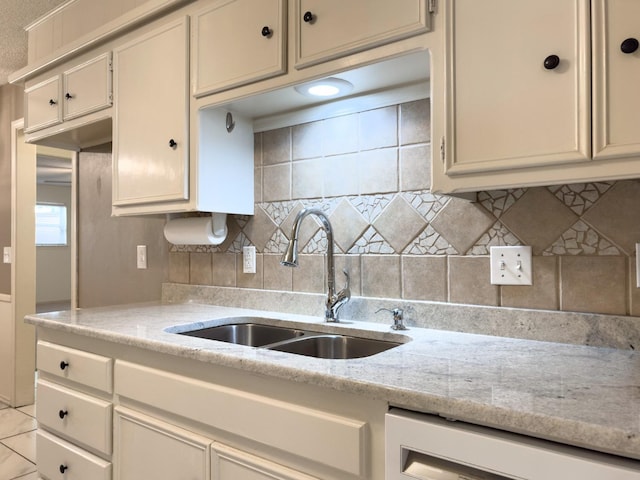 kitchen featuring dishwashing machine, sink, tasteful backsplash, and light stone countertops