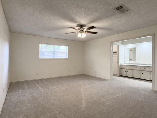 unfurnished bedroom featuring sink, ceiling fan, ensuite bathroom, a textured ceiling, and light colored carpet